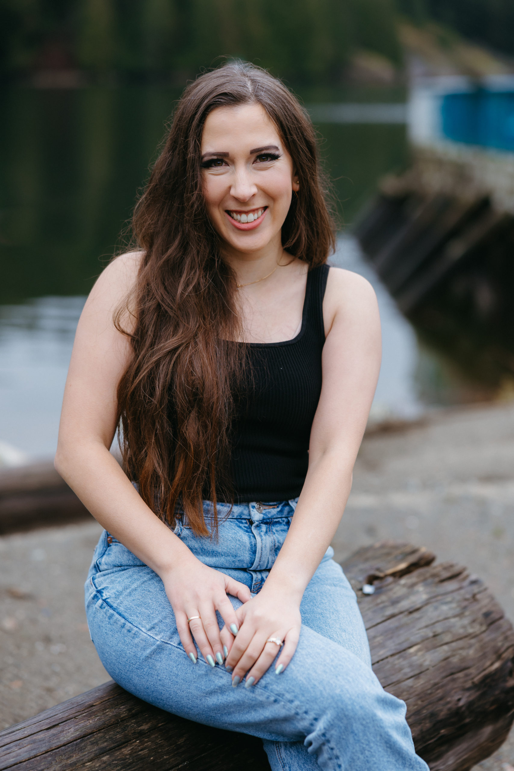 Photo of Ultrasaurus wearing a black tank top and blue jeans sitting on a log in front of a lake